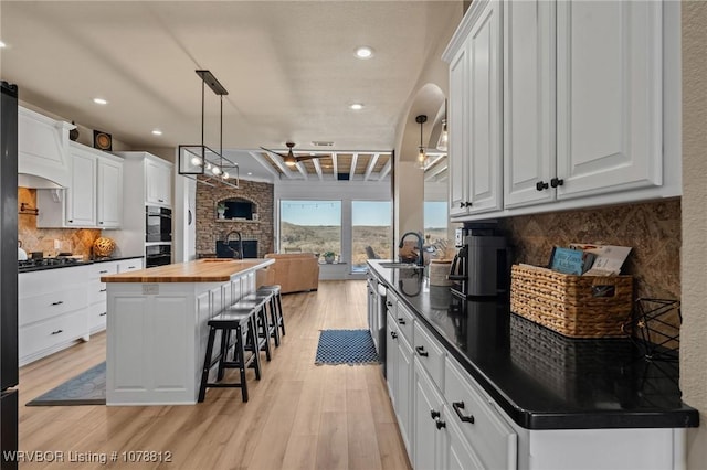 kitchen featuring wood counters, sink, a kitchen island, pendant lighting, and white cabinets