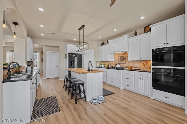 kitchen featuring wood counters, sink, decorative light fixtures, high quality fridge, and white cabinets