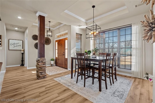 dining room with decorative columns, crown molding, a raised ceiling, and light wood-type flooring