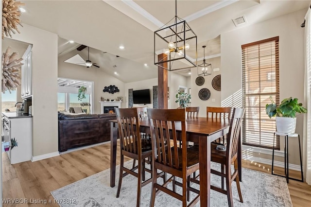 dining space with ornamental molding, lofted ceiling, ceiling fan with notable chandelier, and light wood-type flooring