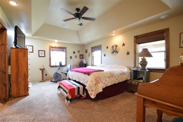 bedroom with light carpet, a tray ceiling, and ceiling fan