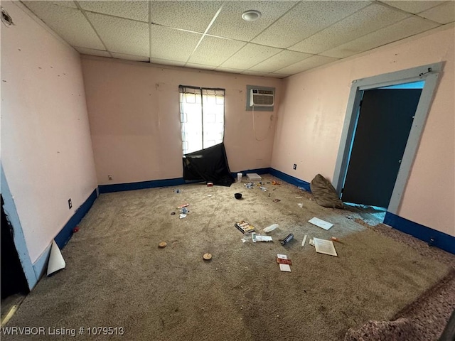 unfurnished room featuring an AC wall unit, baseboards, and a drop ceiling