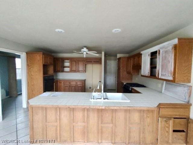 kitchen with light tile patterned floors, ceiling fan, oven, a peninsula, and a sink