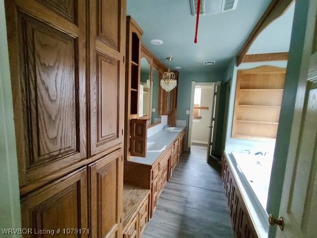 bathroom featuring double vanity, visible vents, wood finished floors, a washtub, and a sink