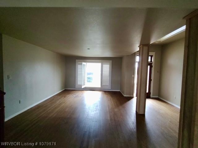 unfurnished room with baseboards and dark wood-type flooring