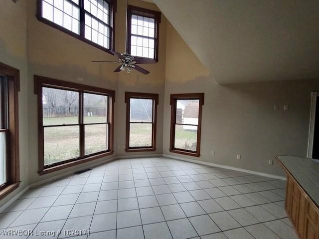 unfurnished living room with light tile patterned floors, a high ceiling, a ceiling fan, and baseboards