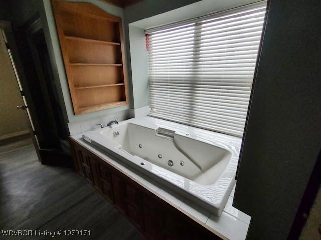 full bath with built in shelves, a jetted tub, and wood finished floors