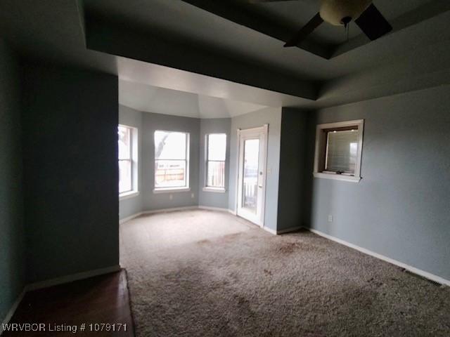 carpeted empty room with a tray ceiling, ceiling fan, and baseboards