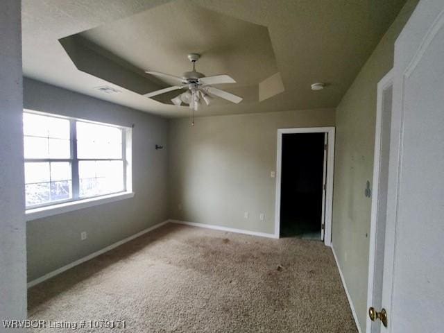 carpeted empty room with a raised ceiling, ceiling fan, and baseboards