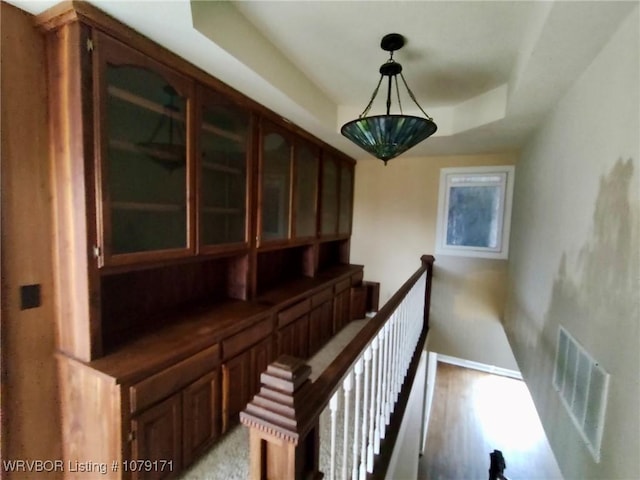 corridor with baseboards, visible vents, a raised ceiling, an upstairs landing, and light wood-style floors