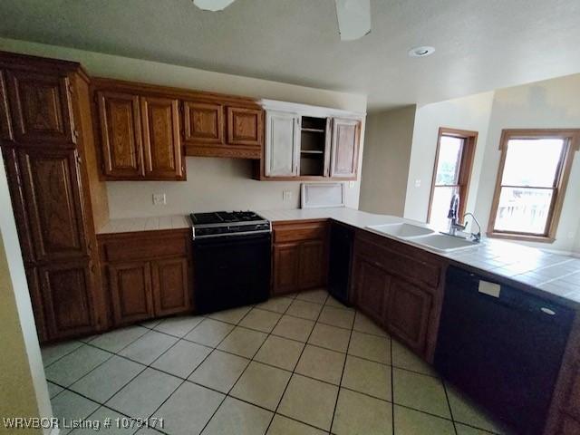 kitchen featuring light tile patterned floors, tile counters, dishwasher, gas range, and a sink