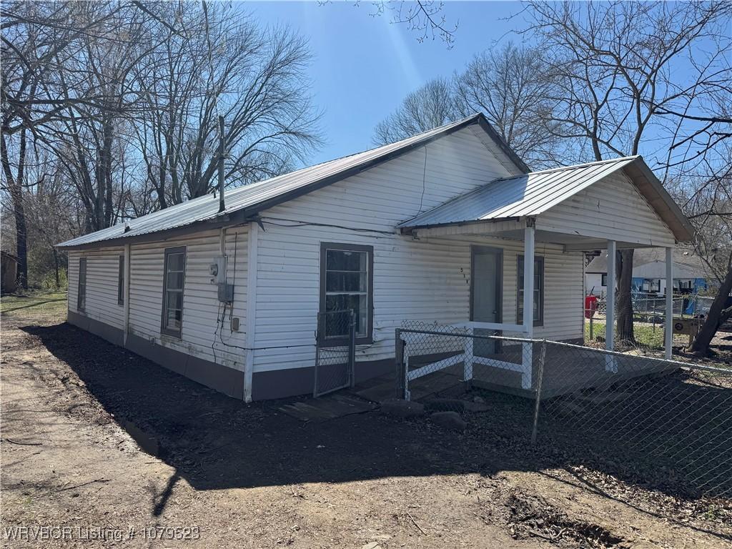 view of side of property featuring metal roof, a porch, and fence