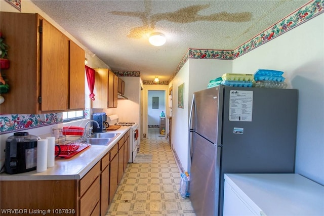 kitchen featuring a textured ceiling, white gas range, sink, and stainless steel refrigerator