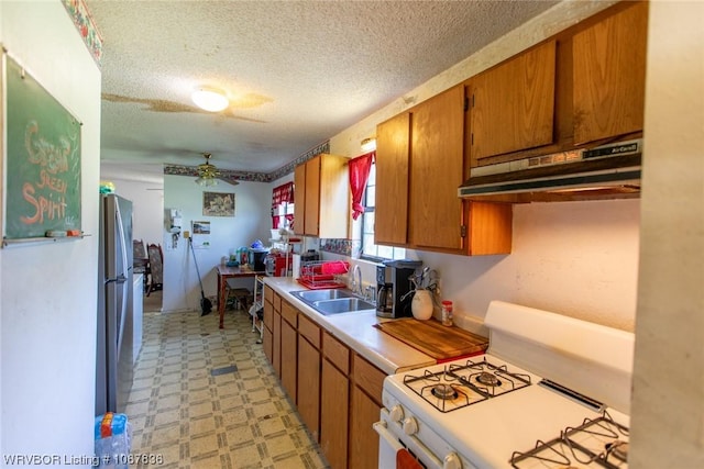 kitchen with ceiling fan, sink, stainless steel fridge, a textured ceiling, and white gas range oven