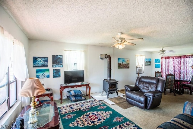 carpeted living room featuring a wood stove, ceiling fan, and a textured ceiling