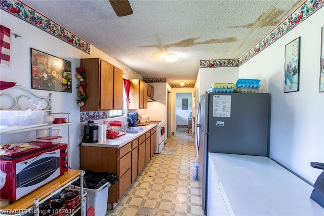 kitchen with a textured ceiling, stainless steel refrigerator, white gas stove, and sink