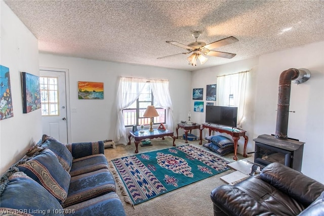 living room with a textured ceiling, a wood stove, ceiling fan, and a healthy amount of sunlight