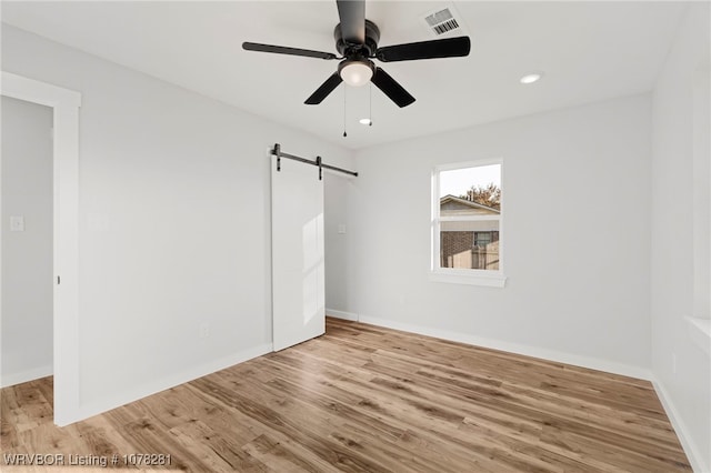 unfurnished bedroom featuring ceiling fan, a barn door, light wood-type flooring, and a closet