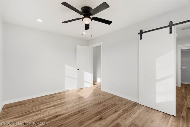 unfurnished bedroom with a barn door, ceiling fan, and light wood-type flooring