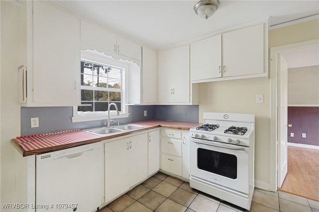 kitchen featuring baseboards, light tile patterned floors, white appliances, white cabinetry, and a sink