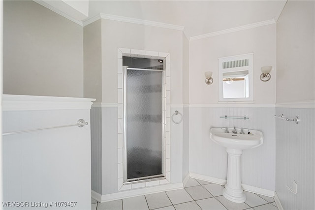 bathroom with a wainscoted wall, a stall shower, tile patterned flooring, and ornamental molding