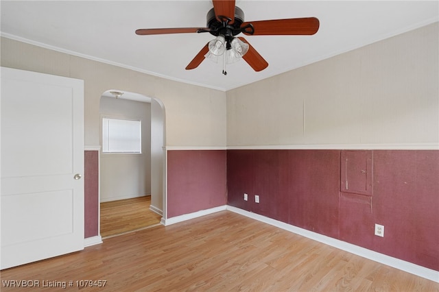 spare room featuring ornamental molding, a ceiling fan, wood finished floors, arched walkways, and baseboards