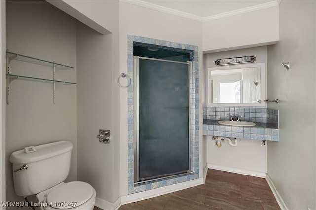 bathroom with crown molding, baseboards, toilet, a stall shower, and a sink