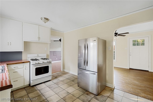 kitchen with white range with gas stovetop, light tile patterned floors, freestanding refrigerator, white cabinetry, and a ceiling fan