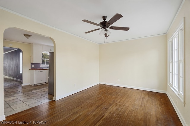 empty room featuring arched walkways, wood finished floors, baseboards, and ornamental molding