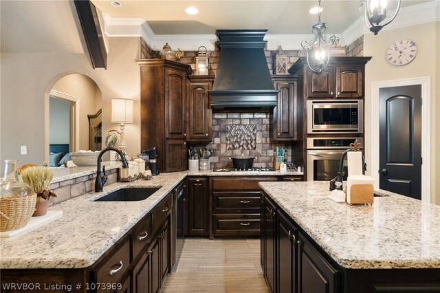 kitchen with appliances with stainless steel finishes, premium range hood, dark brown cabinets, sink, and a center island