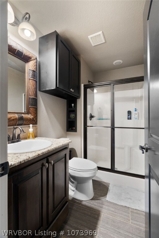 bathroom featuring a shower with door, vanity, a textured ceiling, and toilet