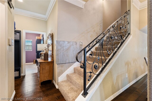 stairway with a barn door, hardwood / wood-style flooring, and ornamental molding