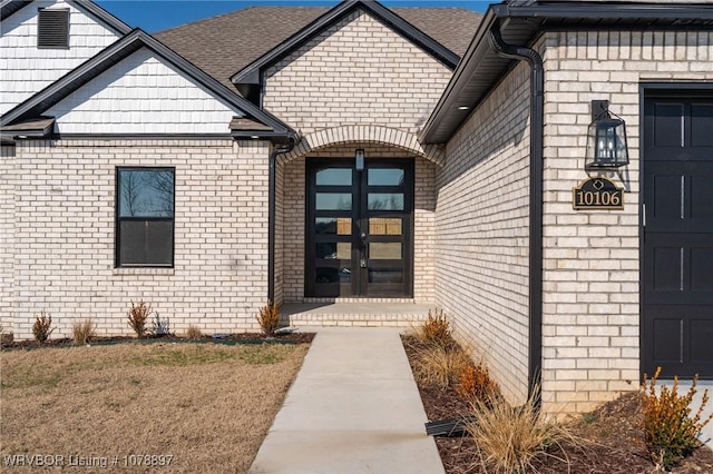 entrance to property with french doors, a shingled roof, and brick siding