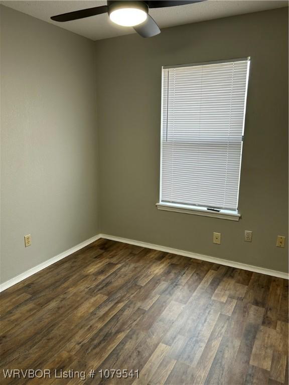 empty room featuring baseboards, dark wood-type flooring, and a ceiling fan