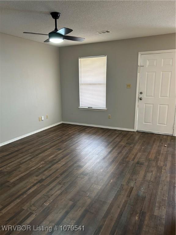 spare room with dark wood-type flooring, a ceiling fan, visible vents, and baseboards