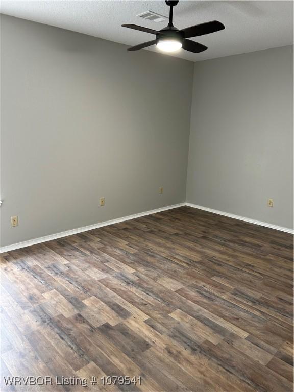 spare room featuring dark wood finished floors, baseboards, visible vents, and ceiling fan