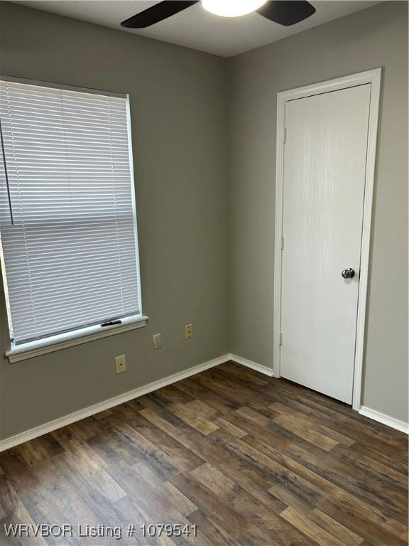 unfurnished room featuring baseboards, dark wood-type flooring, and a ceiling fan