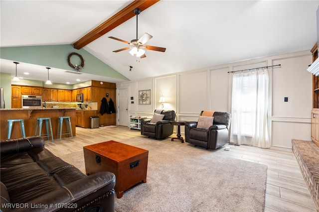 living area with a ceiling fan, a decorative wall, light wood finished floors, and beamed ceiling