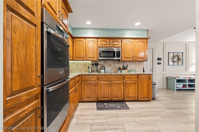 kitchen with stainless steel appliances, brown cabinets, backsplash, and light stone counters