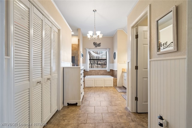 full bath with a garden tub, crown molding, a closet, an inviting chandelier, and wainscoting