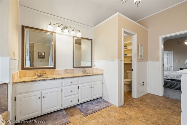 ensuite bathroom featuring double vanity, toilet, a wainscoted wall, ensuite bath, and a sink