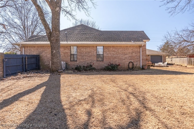 view of property exterior featuring a shingled roof, brick siding, and fence