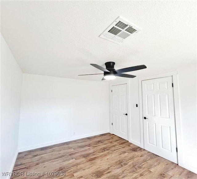 unfurnished bedroom featuring visible vents, baseboards, a textured ceiling, and wood finished floors