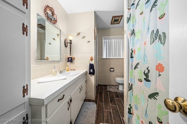 bathroom with toilet, tile walls, walk in shower, and vanity