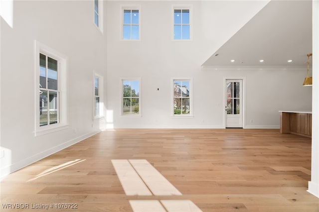 unfurnished living room featuring plenty of natural light, light hardwood / wood-style floors, and a high ceiling