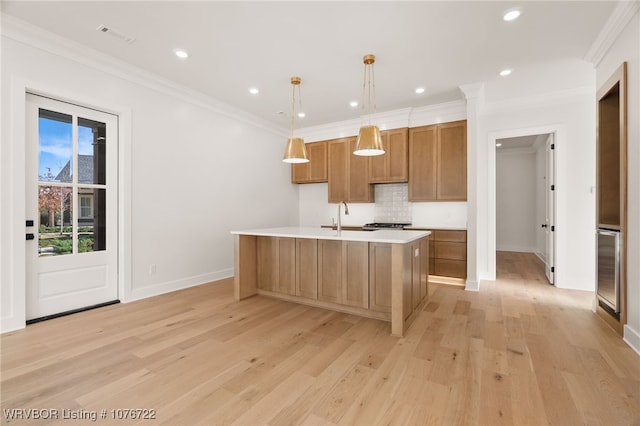 kitchen with a center island with sink, light hardwood / wood-style flooring, hanging light fixtures, and ornamental molding