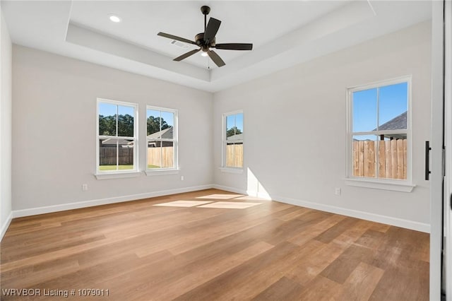 empty room with a raised ceiling, ceiling fan, and light wood-type flooring