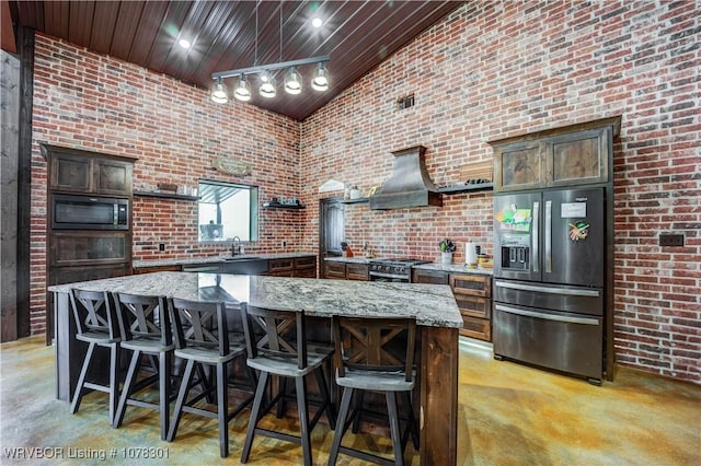 kitchen with appliances with stainless steel finishes, a center island, light stone counters, and dark brown cabinetry