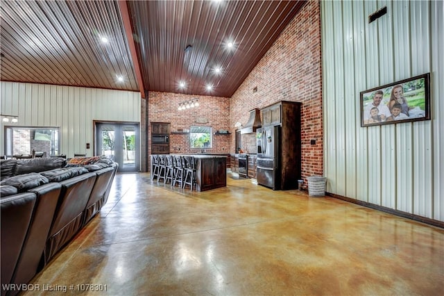 kitchen with stainless steel fridge, a kitchen breakfast bar, brick wall, high vaulted ceiling, and a kitchen island