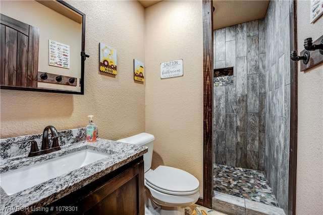 bathroom with tiled shower, vanity, and toilet